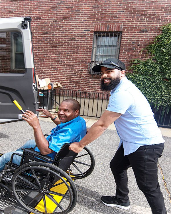 A disabled person in a wheelchair with his attendant, both smiling.