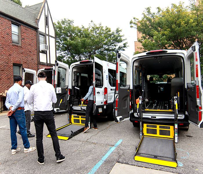 Four attendants positioned near an ambulette with its rear door open, coordinating to assist a passenger safely and efficiently.