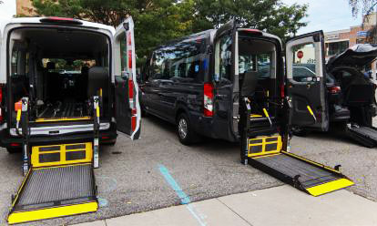Two ambulette vans with open back doors, prepared for safe wheelchair and passenger boarding.