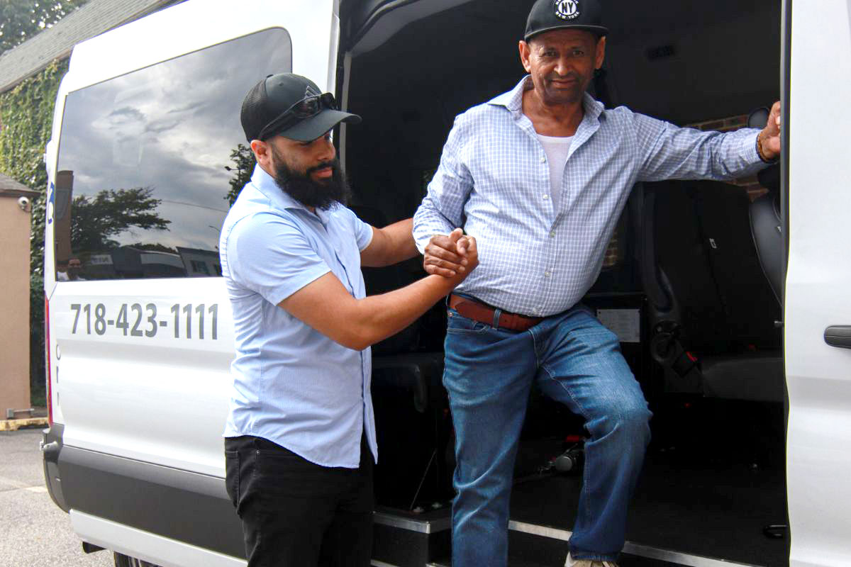 A trained attendant helps an elderly passenger step out of an ambulette with care and support.